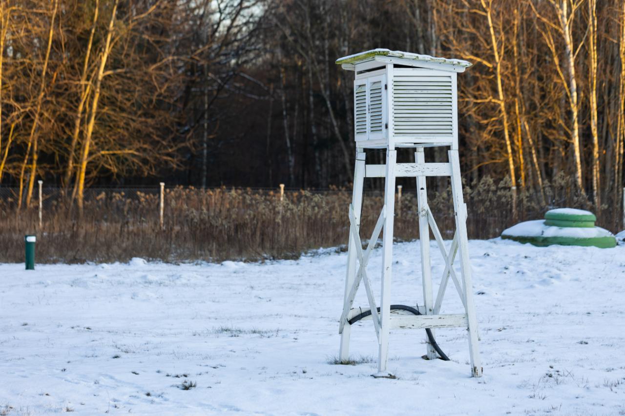 A white louvered thermometer shelter on tall legs, standing in a snowy field.
