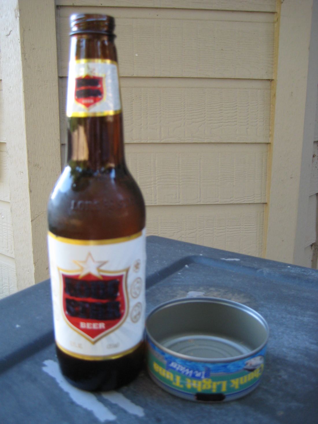A bottle of beer beside an empty, washed-out tuna can.
